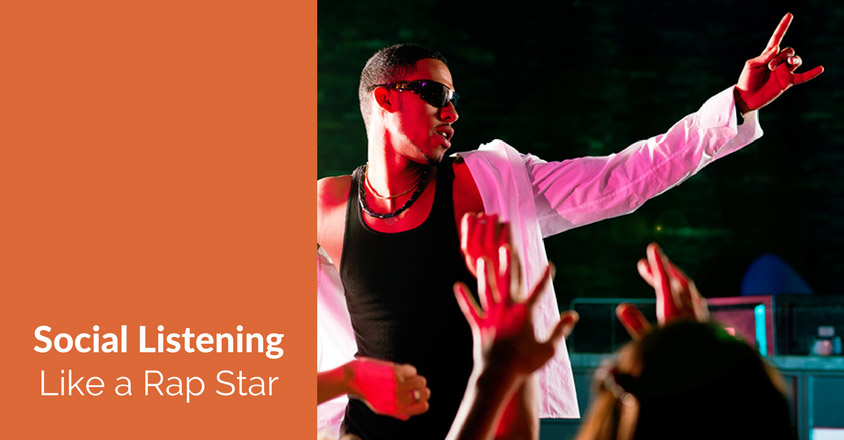 The image is split into two sections. On the left, an orange background displays white text that reads, "Social Listening Like a Rap Star." On the right side, a vibrant photo of a rapper performing on stage is shown, dressed in a black tank top and white jacket, wearing sunglasses, and engaging with the crowd by gesturing with his hand. The audience's hands are raised in response, indicating an energetic performance. The rapper's interaction with the audience is a visual metaphor for "social listening," suggesting the importance of paying attention and engaging with an audience on social media, much like how a performer responds to the crowd during a live show. The overall design is dynamic and bold, reflecting the concept of active listening and engagement.