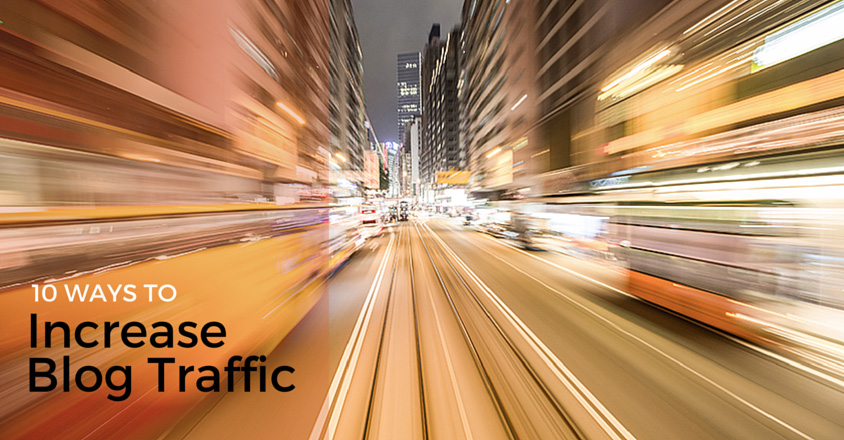 The image shows a dynamic, blurred view of a city street at night, capturing the sensation of motion and speed. Buildings and lights on both sides of the street appear stretched, emphasizing the fast-paced movement. The lines of the street lead the viewer’s eye toward the center, creating a sense of direction and progress. On the left side, text in black reads, "10 Ways to Increase Blog Traffic," suggesting the image is part of a guide or article focused on driving online engagement. The combination of the fast motion and the urban setting visually represents the idea of accelerating blog growth and increasing traffic. 