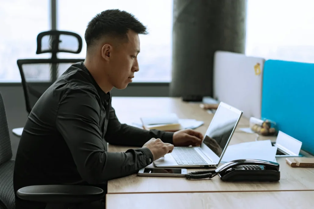 Person typing on a laptop at a desk with papers and a desk phone.