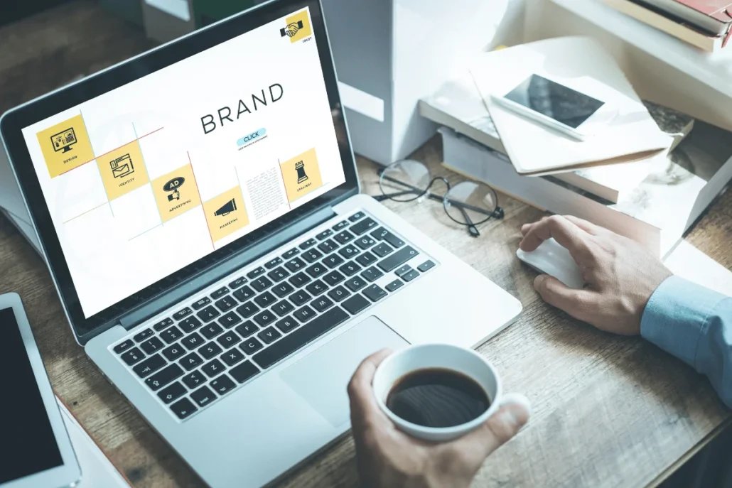 Person working on a laptop with a branding presentation on the screen, holding a cup of coffee.