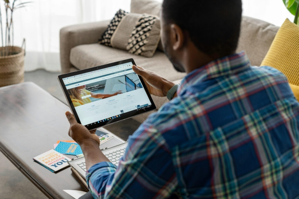 Person using a tablet with a website open, sitting at a table with a laptop and notebook.