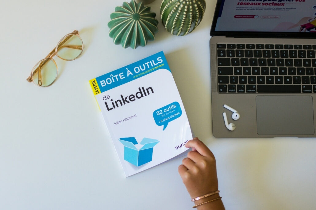 Desk with LinkedIn guidebook, laptop, glasses, decorative plants, and earphones.