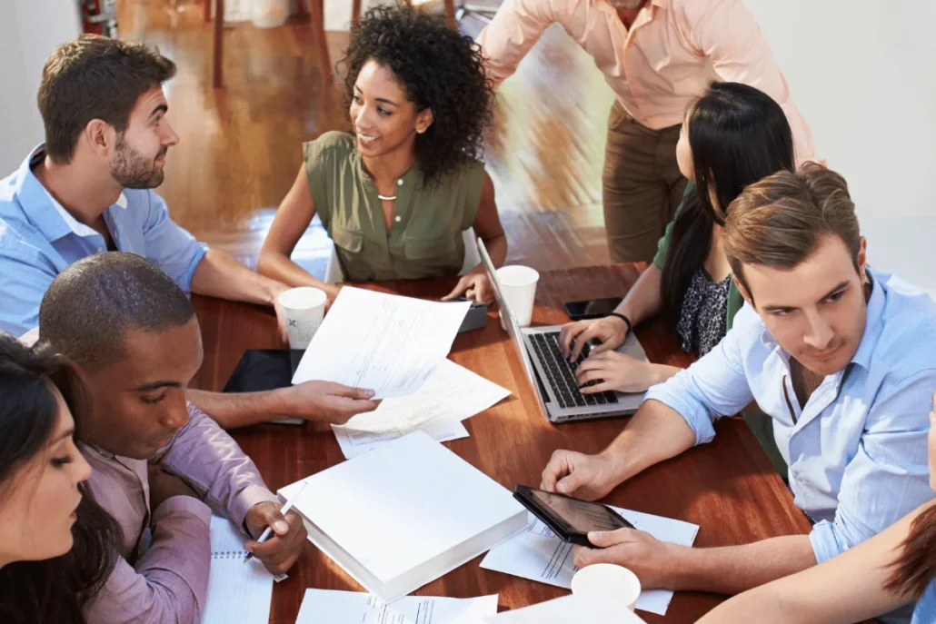 Group of professionals engaged in a meeting with documents and laptops on a table.