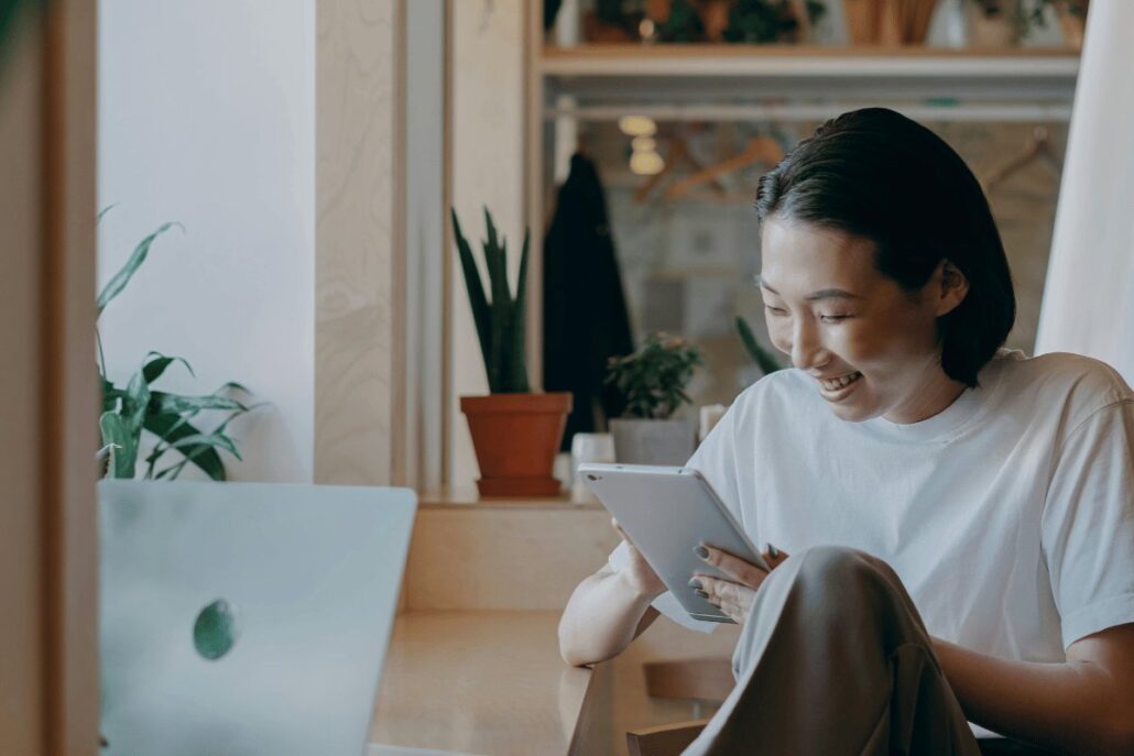 Person sitting by a laptop with a tablet in a cozy room with plants.