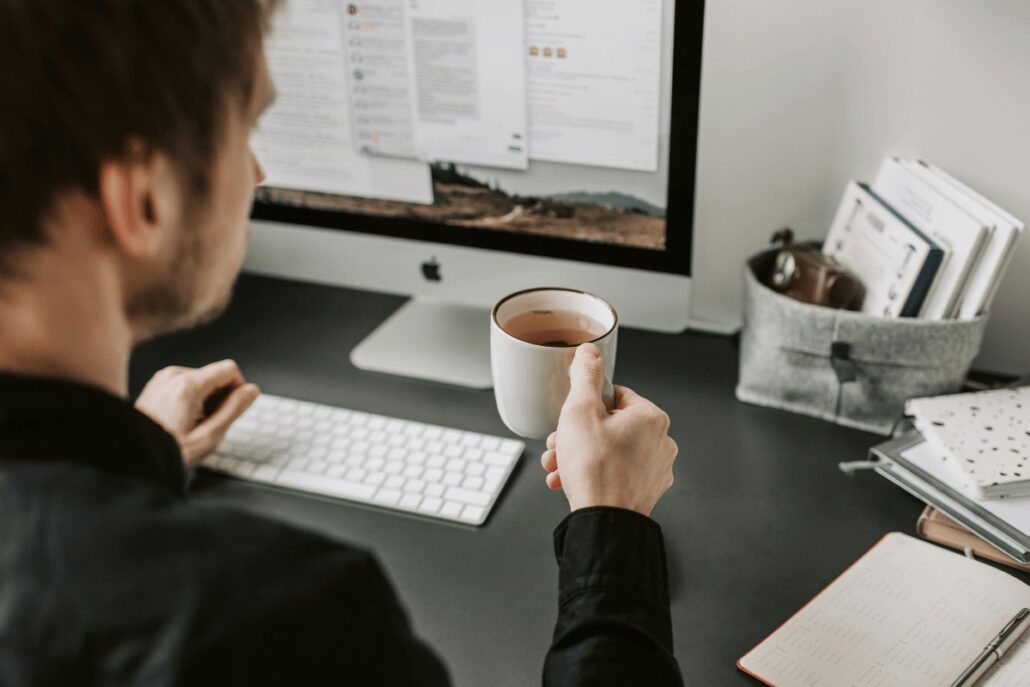 A man holding a cup of tea while sitting in front of a computer screen, focused on his work.