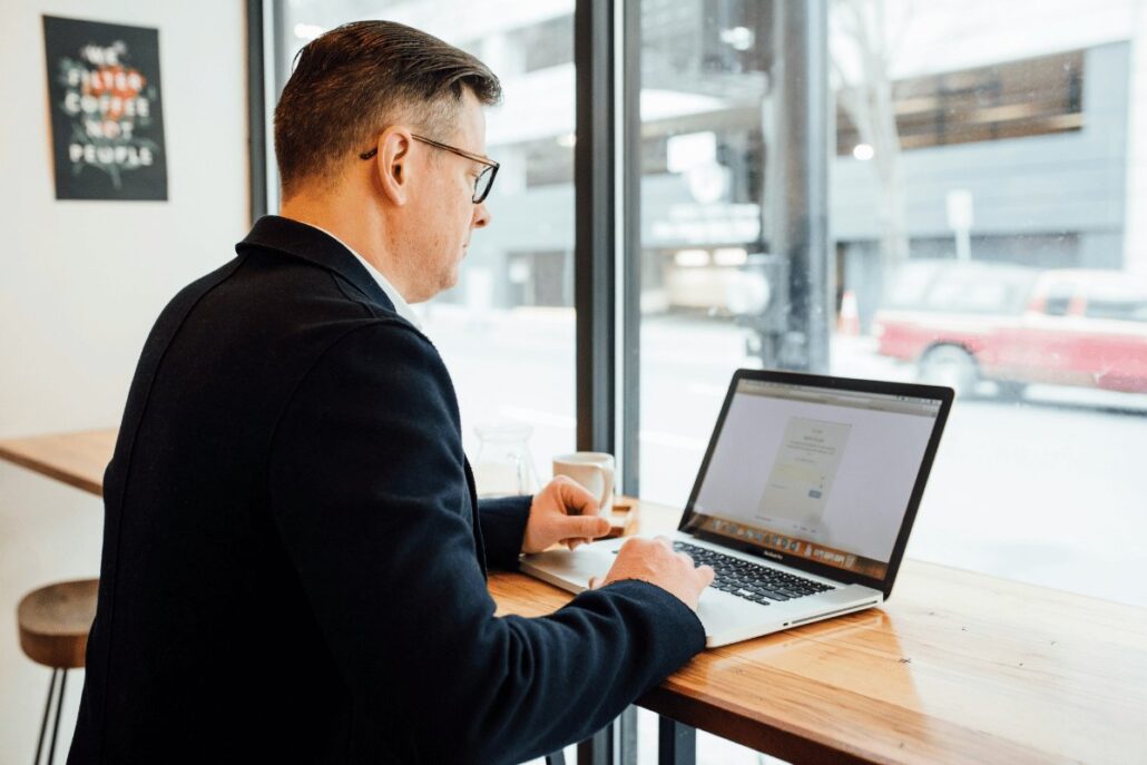 A man in a suit is seated at a table, working on a laptop, focused and engaged in his task.