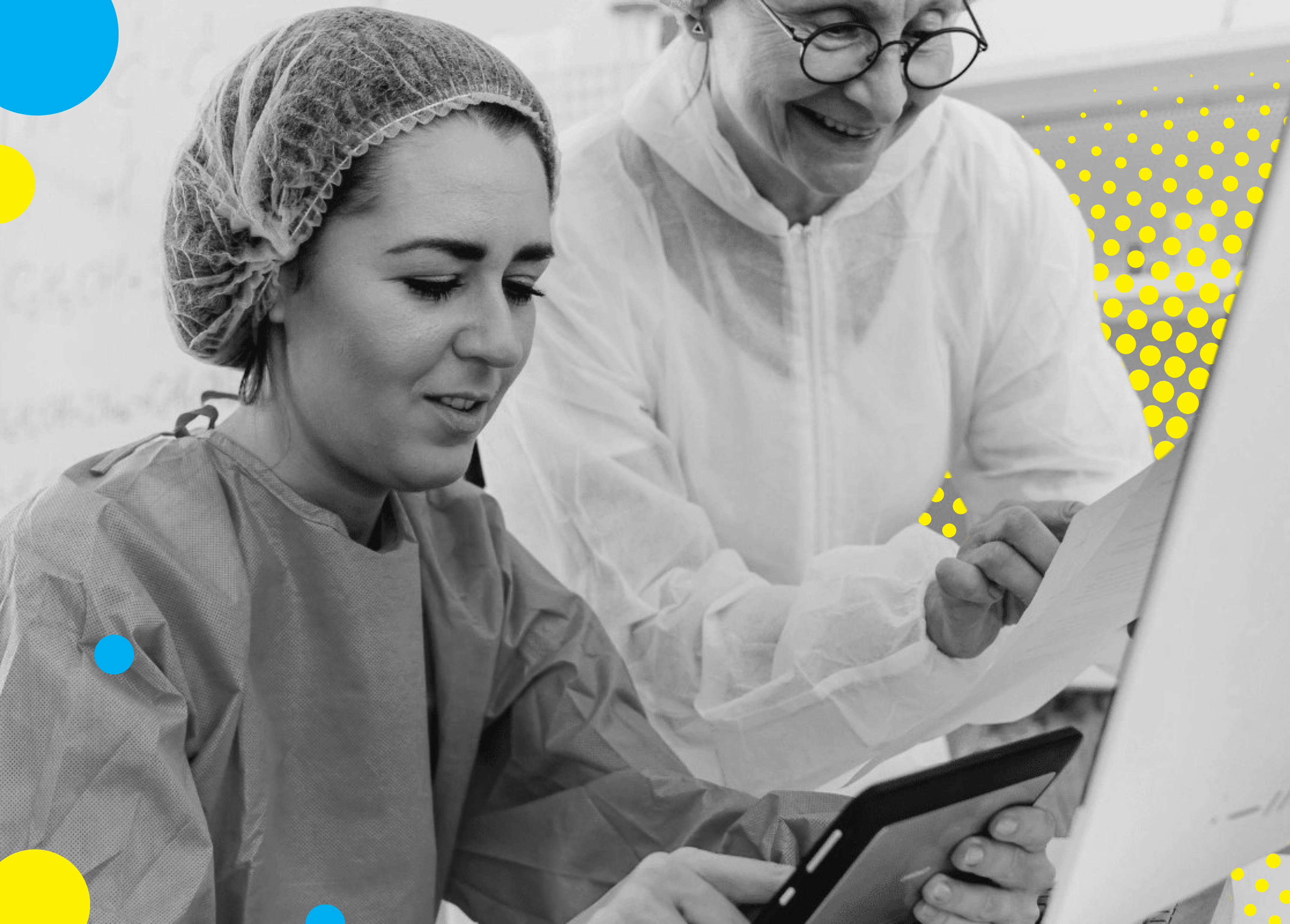 Two healthcare professionals in PPE discussing over documents and a tablet.