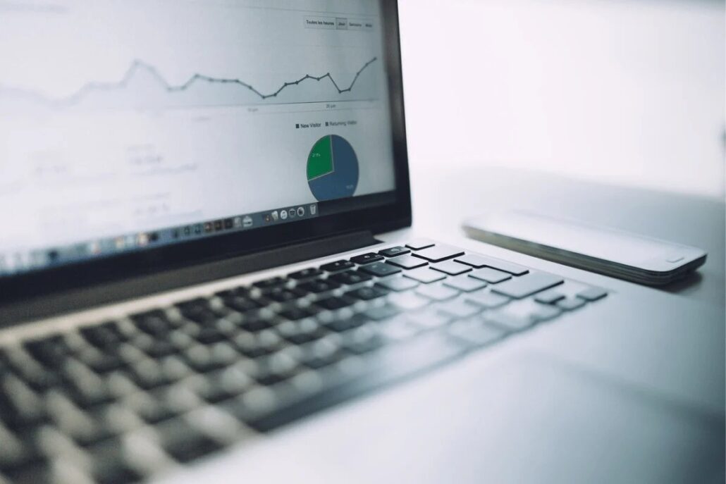 Laptop with analytics on the screen beside a smartphone on a white desk.