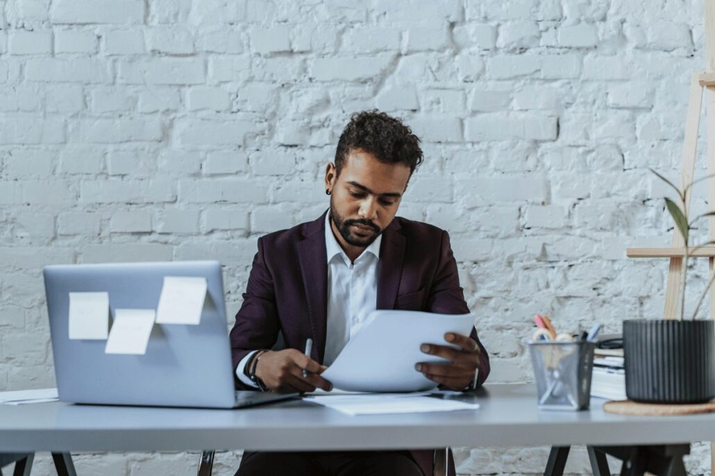 Person in a suit working with documents at an office desk with laptop and stationery.