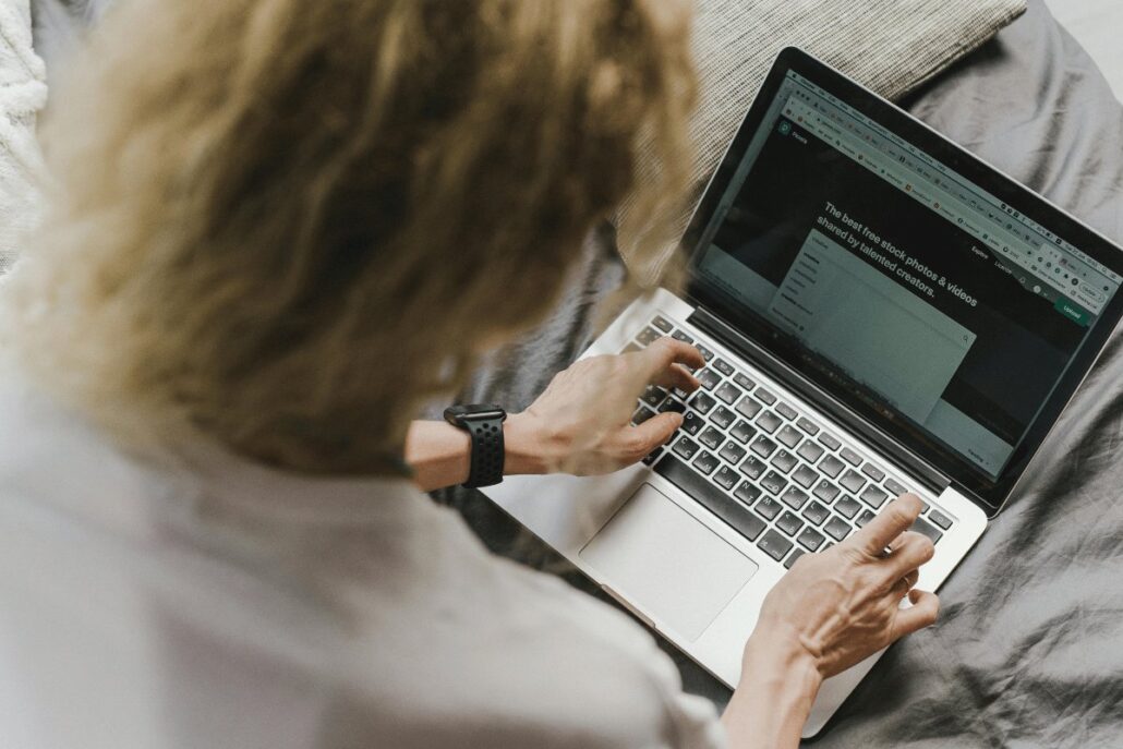 Person using a laptop on a bed with a website open on the screen.