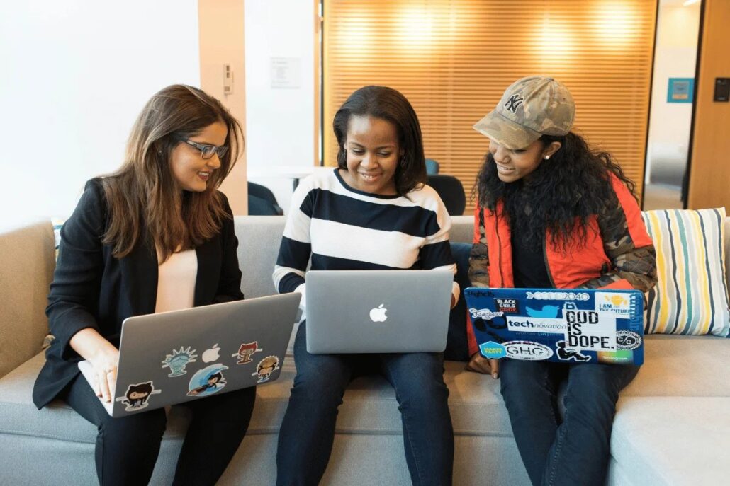 Three individuals sitting on a couch with laptops, engaged in a discussion.