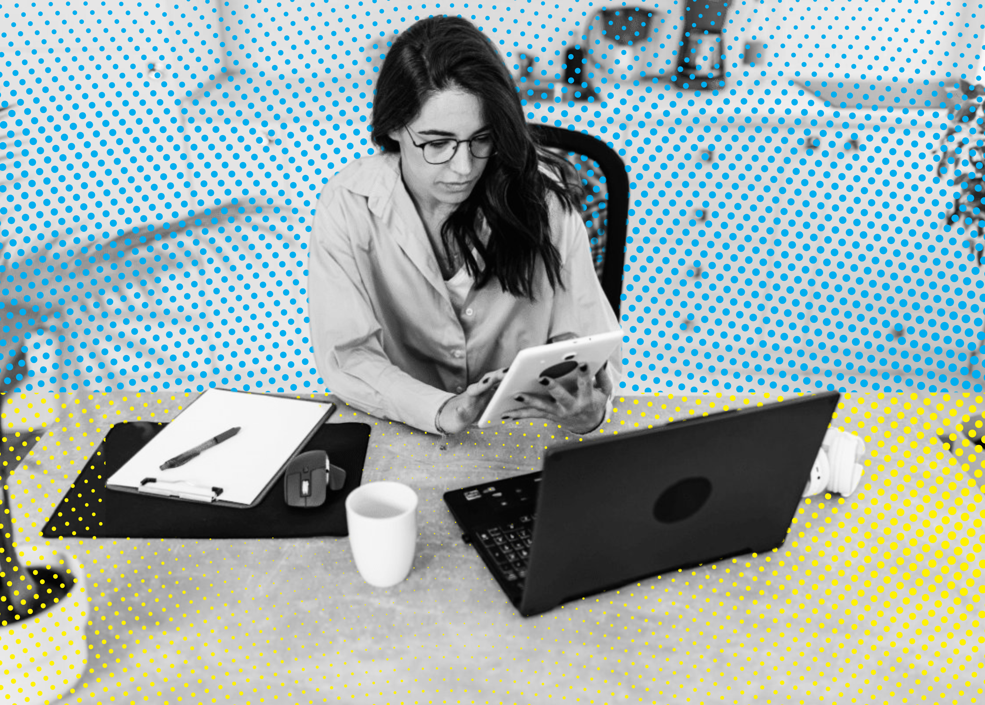 Woman in blue shirt using tablet at desk with laptop, clipboard, and coffee cup.