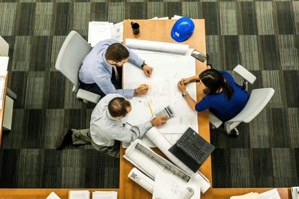 Three professionals examining architectural plans on a table from above.