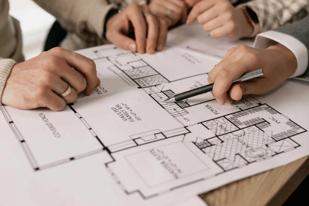 Several hands reviewing and drawing on architectural blueprints on a table.