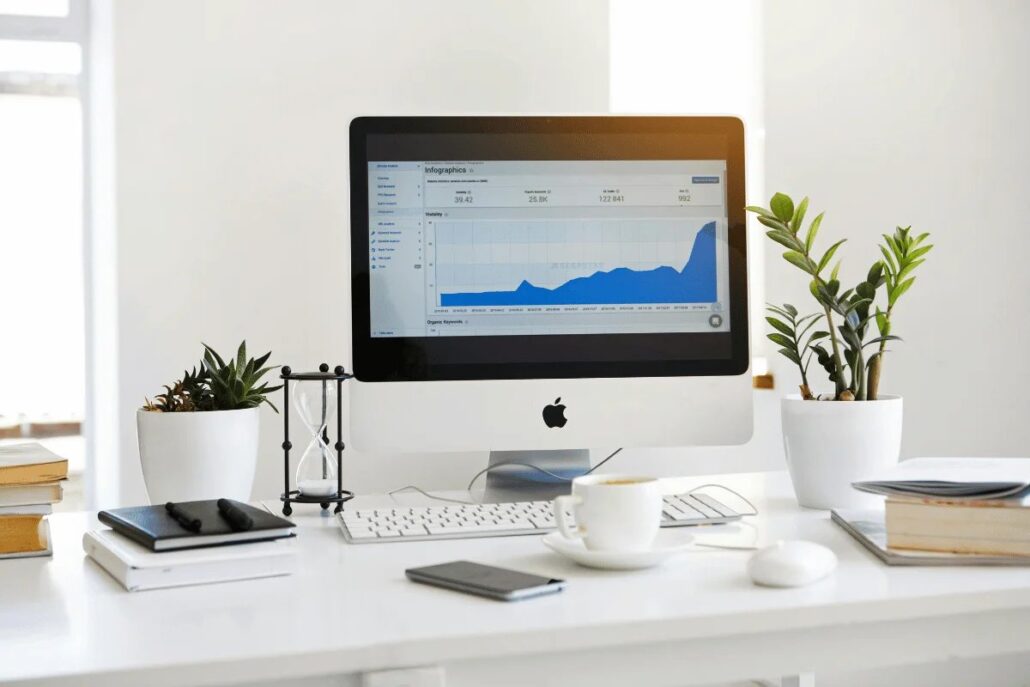 Modern workspace with iMac displaying graphs, coffee cup, and indoor plants.