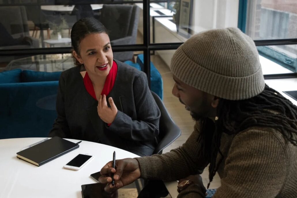 Two people having a discussion at a table with notebooks and a smartphone.