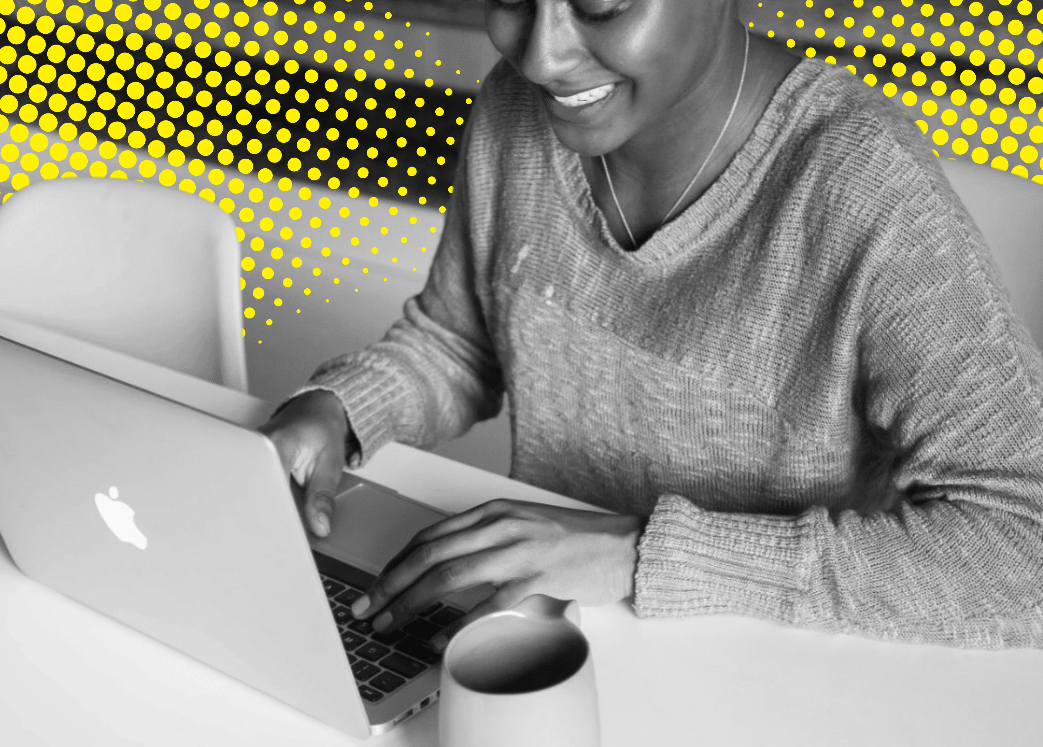 A person in a cozy gray sweater types on a laptop at a table, with a coffee mug nearby and a vibrant, dotted yellow background.