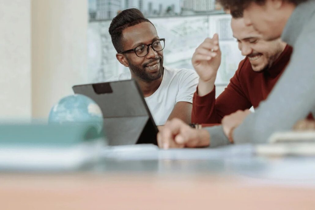 A group of people is discussing ideas around a table, with a globe and a tablet in view, emphasizing collaboration and brainstorming.