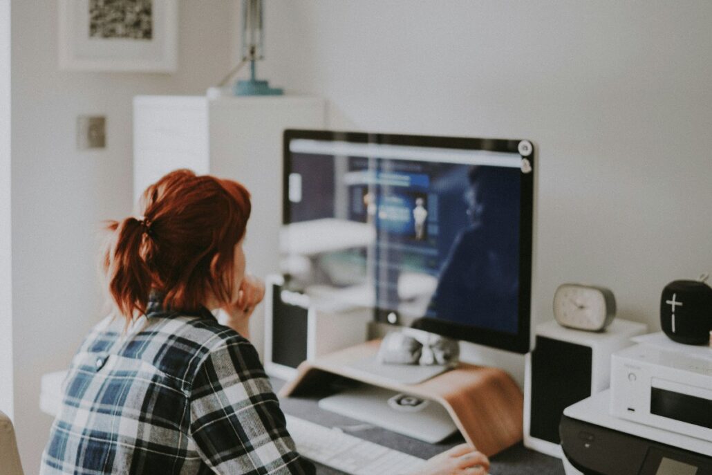 Freelancer or remote worker with red hair using a desktop computer in a cozy home office.