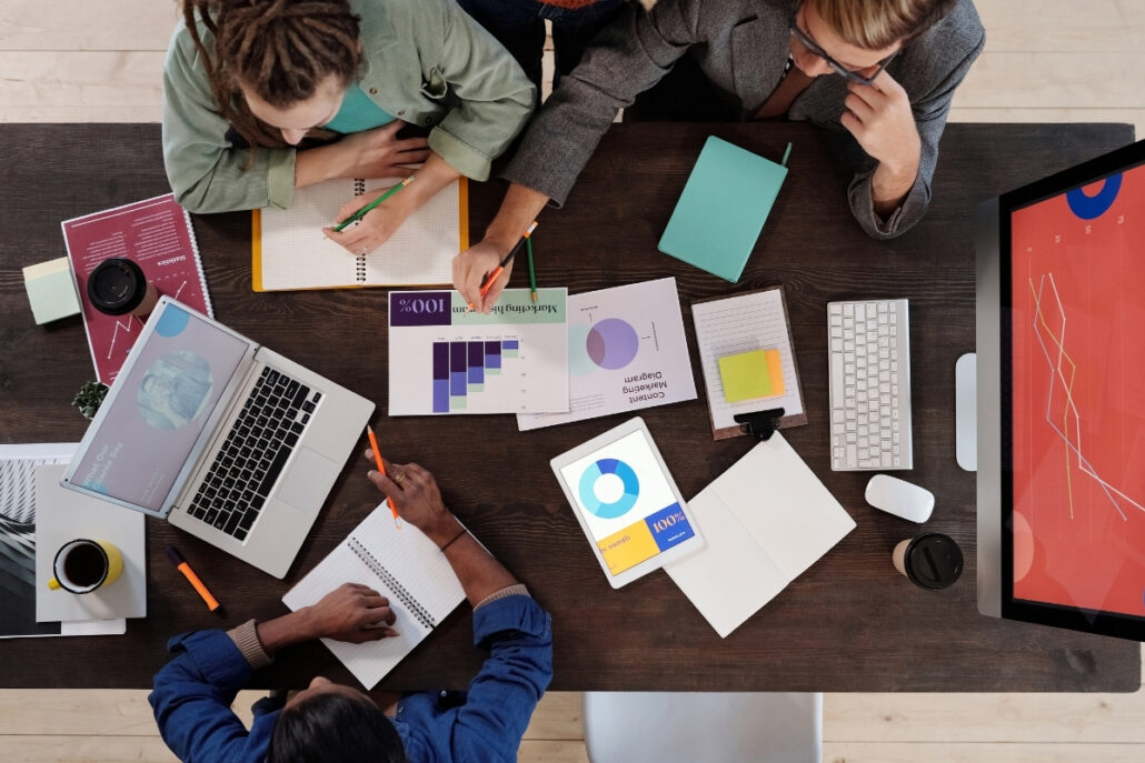 Overhead view of colleagues brainstorming around a table with charts, laptops, and notebooks.