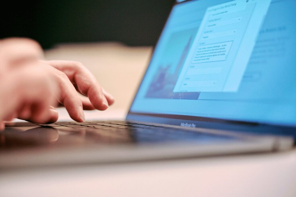 Close-up shot of a hand typing on a MacBook Pro with a web page open on the screen.