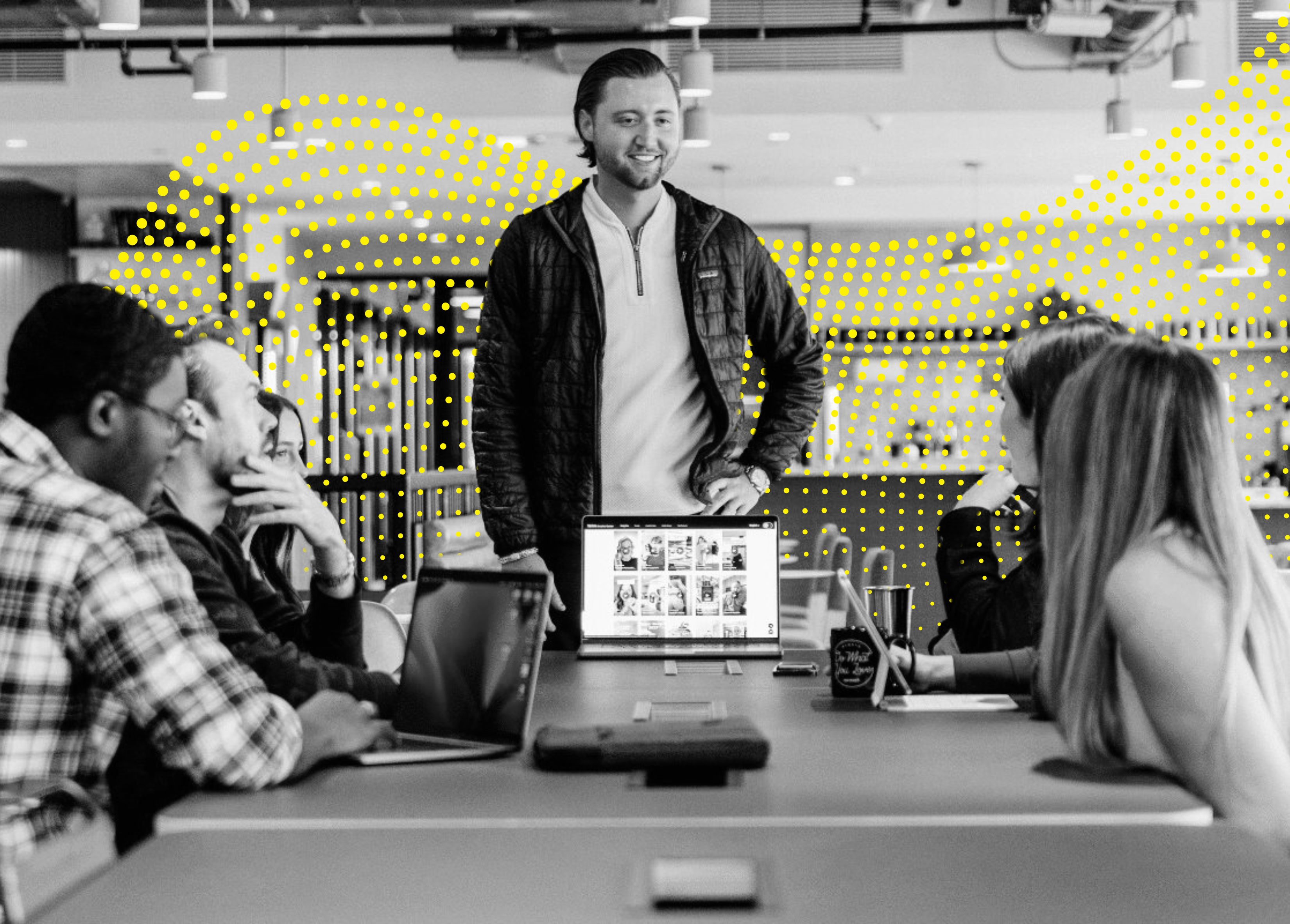 A group of people engaged in a discussion around a conference table, with a laptop displaying images in the center.