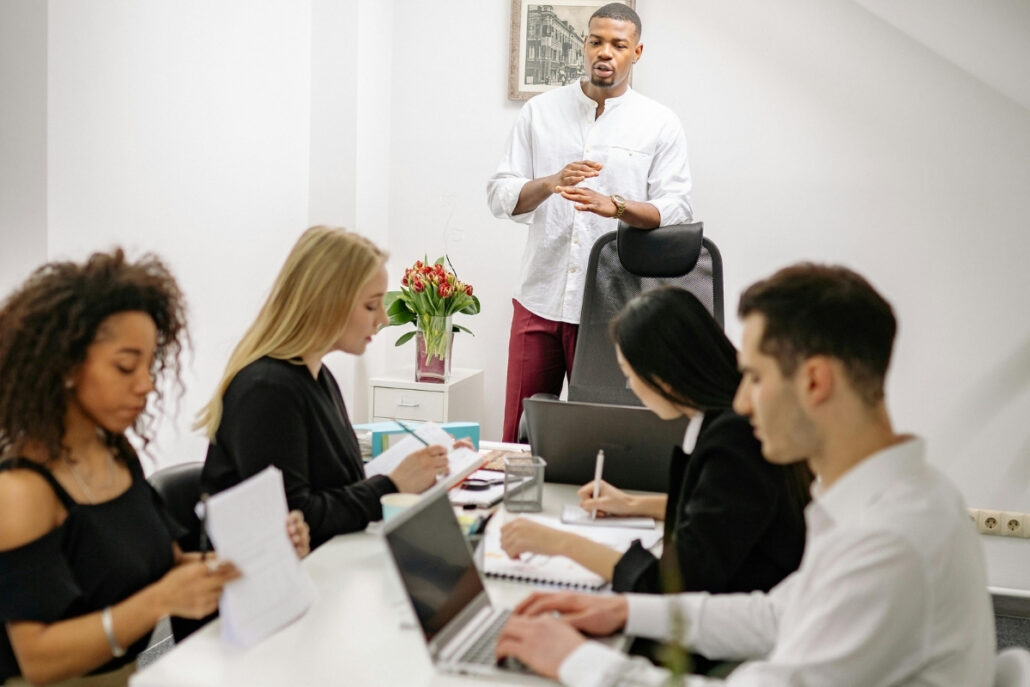 A team of professionals engaged in a meeting led by a presenter in a white shirt.