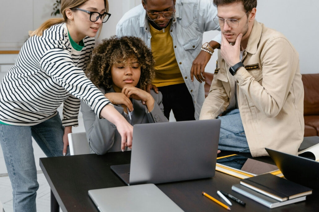 Diverse team collaborating on a project, with one member pointing to a laptop screen.