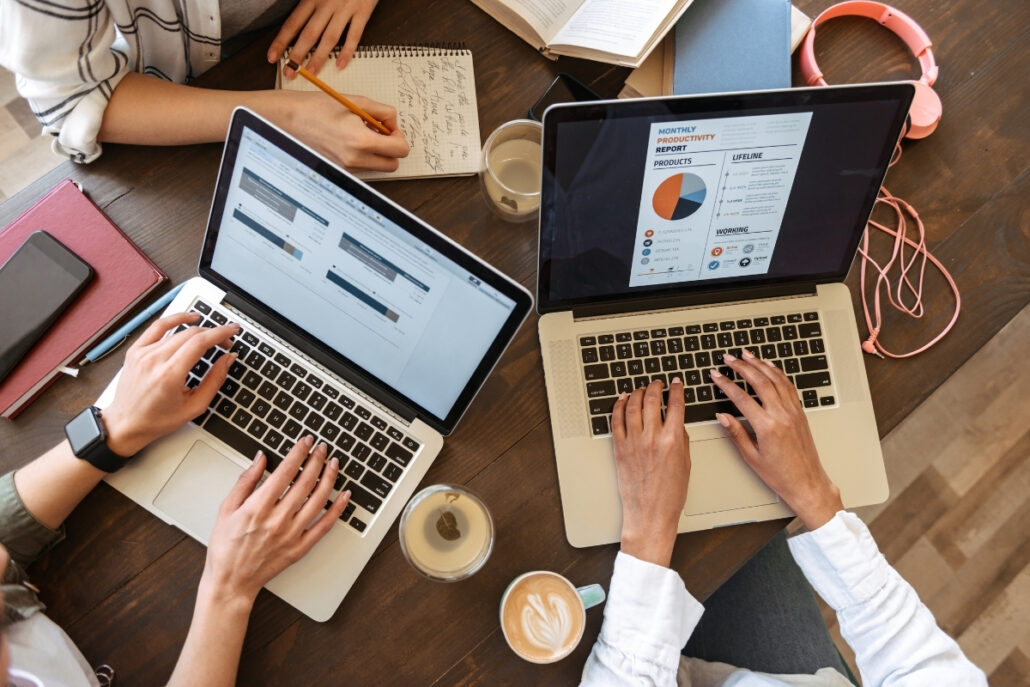 Collaborative workspace with laptops, notebooks, and coffee on a shared desk.
