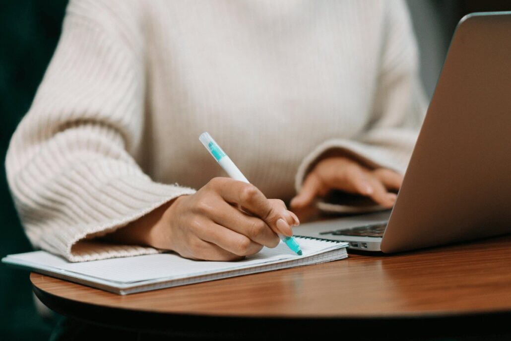 A person writing in a notebook while using a laptop.