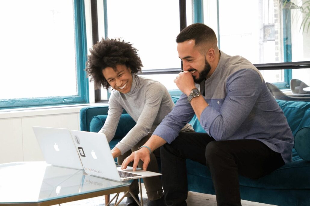 Two coworkers smiling while collaborating on laptops.