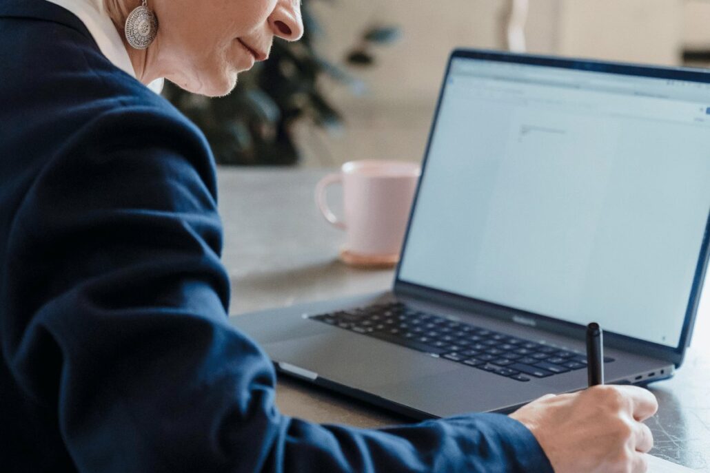 Businesswoman writing notes beside a laptop on a desk.