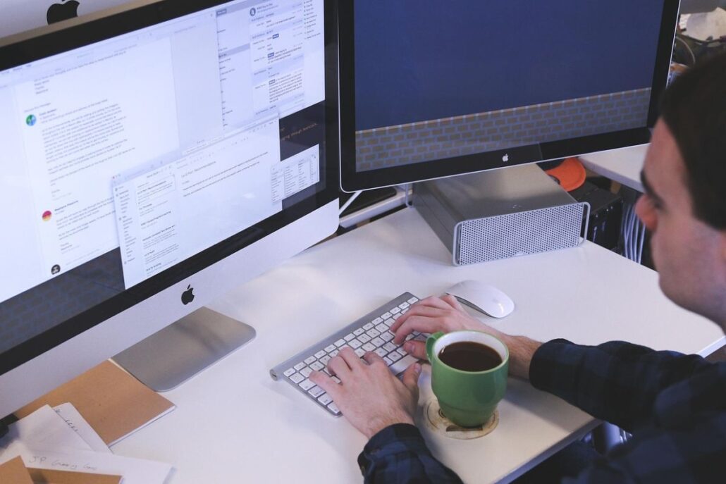 Man working at a dual-screen desktop with a green coffee mug.