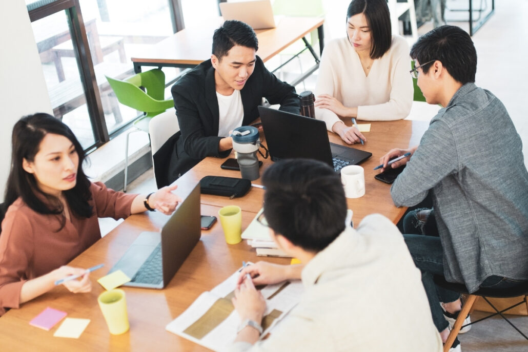 A team of young professionals having a discussion around a wooden table in a bright office.